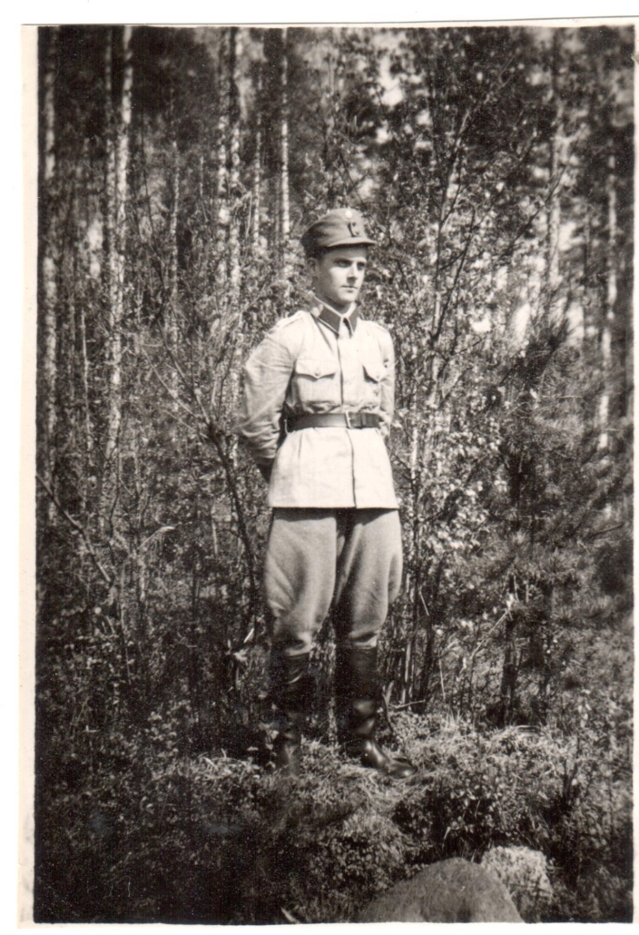 Mustavalkoisessa kuvassa sotilas seisoo metsän reunassa.