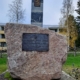 Kuvassa suurikokoinen muistomerkkikivi, jossa tekstilaatta ja Suomen sinivalkoinen rajapaalu.