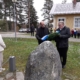 Kuvassa kaksi miestä laskemassa seppelettä muistomerkille. Yleisönä mm. oppilaita.