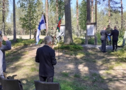 kuvassa ihmisiä ja lippuja maanpuolustusjuhlassa.