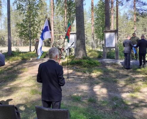 kuvassa ihmisiä ja lippuja maanpuolustusjuhlassa.