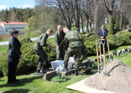 Kolme varusmiestä maastopuvuissa laskee valkoista pienoisarkkua hautaan