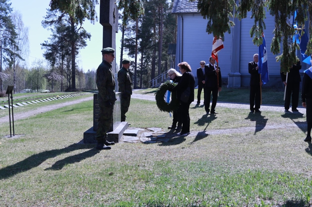 Kuvassa seppeleenlaskijat, lippulinna ja kunniavartio. Taustalla kirkko ja sankarihautoja.