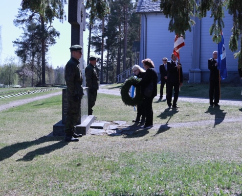Kuvassa seppeleenlaskijat, lippulinna ja kunniavartio. Taustalla kirkko ja sankarihautoja.