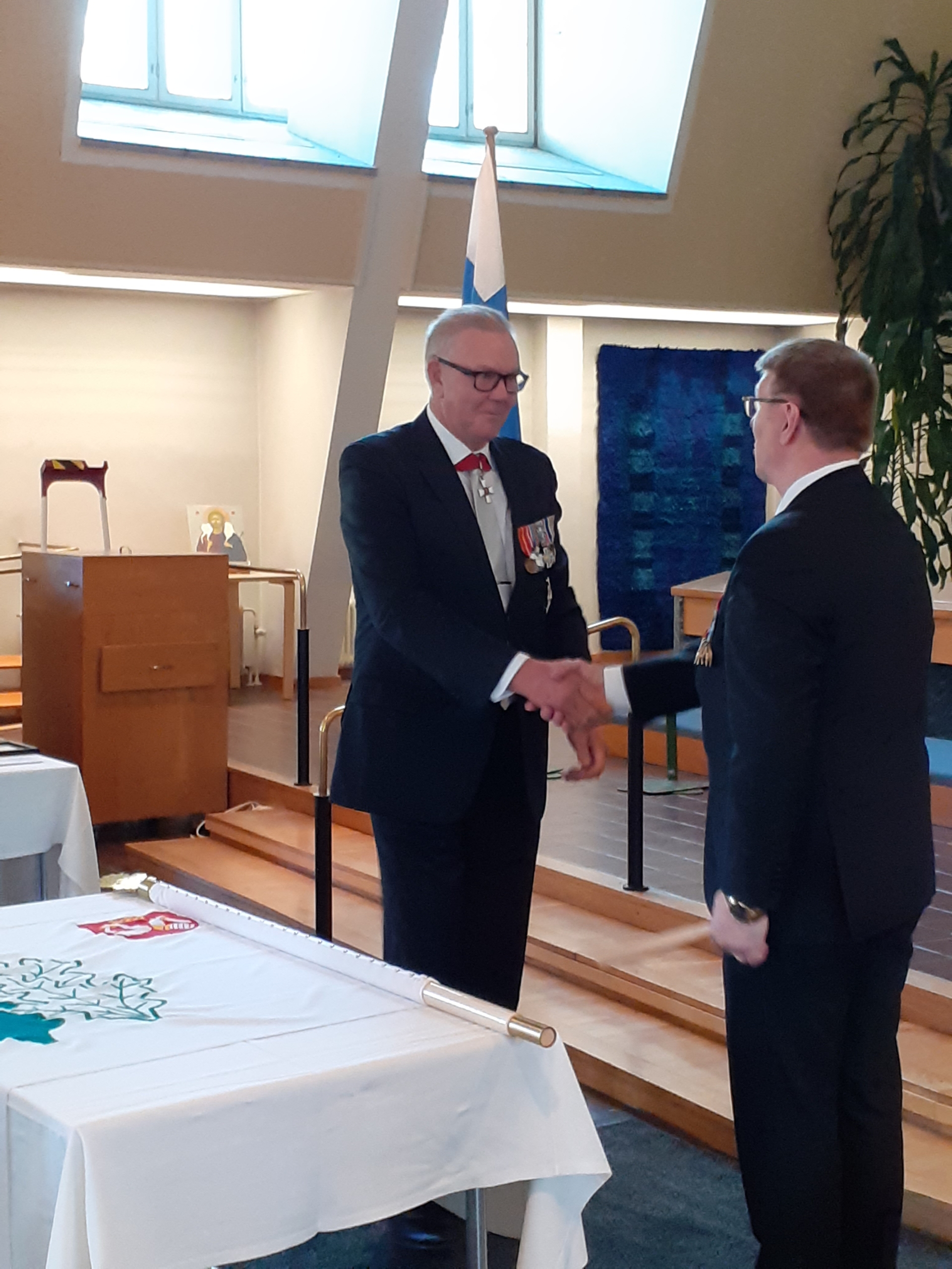 Kuvassa mieshenkilöt kättelevät lipun äärellä.