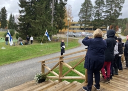 Kuvassa tilaisuuden osallistujia, muistomerkki ja Suomen liput.