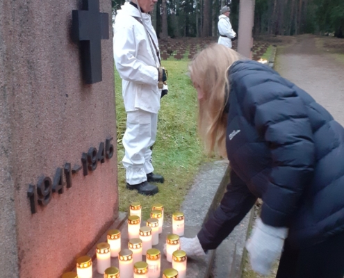 Kuvassa lasketaan kynttilä sankarihaudan muistomerkille. Taustalla kunniavartio.