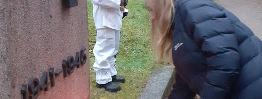 Kuvassa lasketaan kynttilä sankarihaudan muistomerkille. Taustalla kunniavartio.