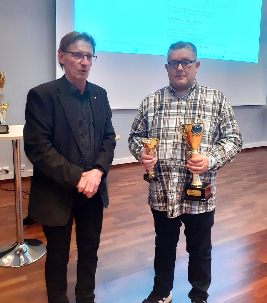 Kuvassa kaksi mieshenkilöä. Toisella käsissään kaksi palkintopokaalia.