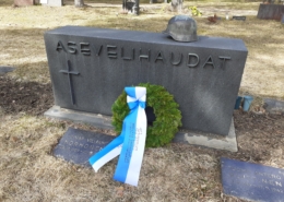 Kuvassa hautamuistomerkki, jonka päällä sotilaskypärä.