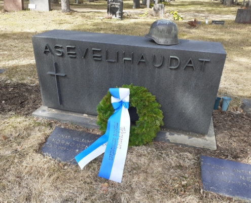 Kuvassa hautamuistomerkki, jonka päällä sotilaskypärä.