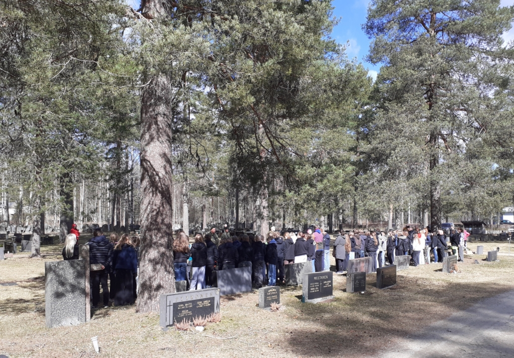 Kuvassa ihmisjoukko ryhmittyneenä hautausmaalle.