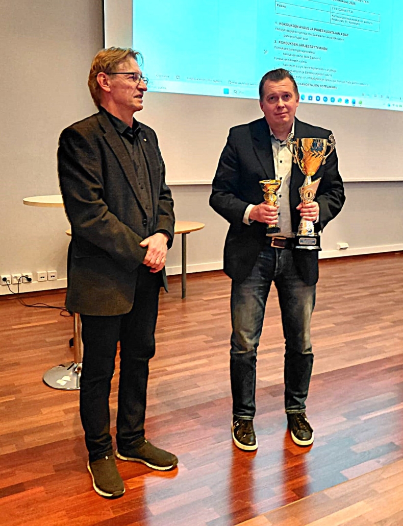Kuvassa kaksi mieshenkilöä. Toisella käsissä kaksi palkintopokaalia.