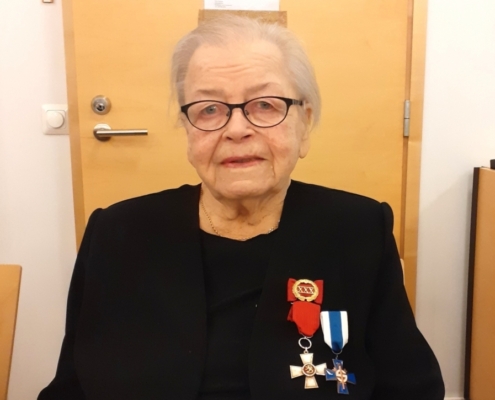 Kuvassa naispuolinen veteraani, kunniamerkit rinnassa.