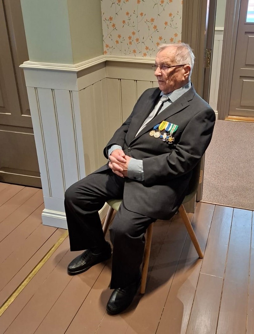 Kuvassa mies istumassa, kunniamerkit rinnassa.