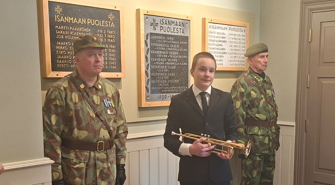 Kuvassa soittaja instrumentin kanssa. Taustalla reserviläisten kunniavartio ja pro patria -taulut.