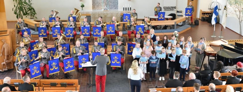 Kuvassa sotilassoittokunta ja lapsikuoro esiintymässä.